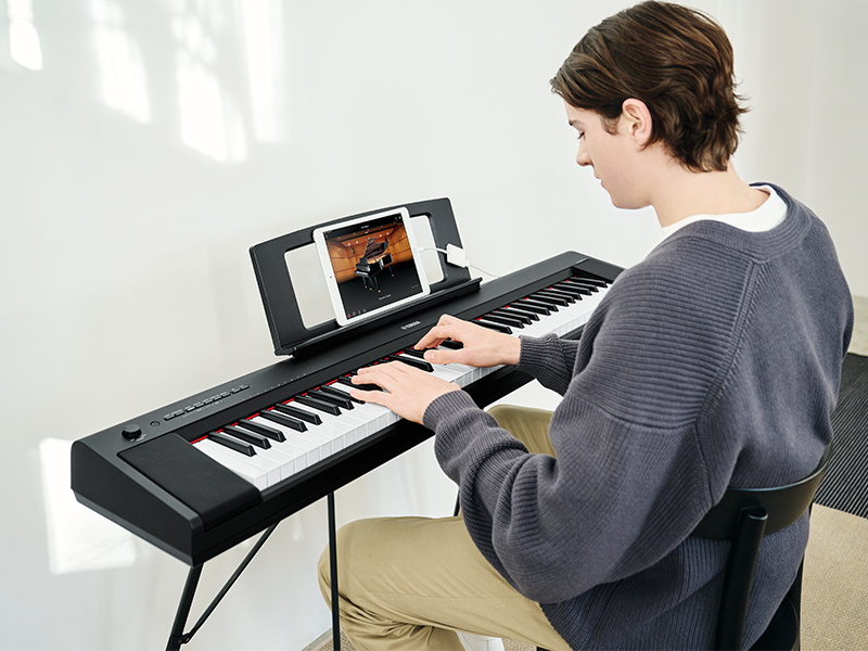 Man playing NP-15B on L-2C stand connected to Smart Pianist on iPad